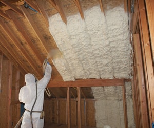 A man spraying insulation on a ceiling